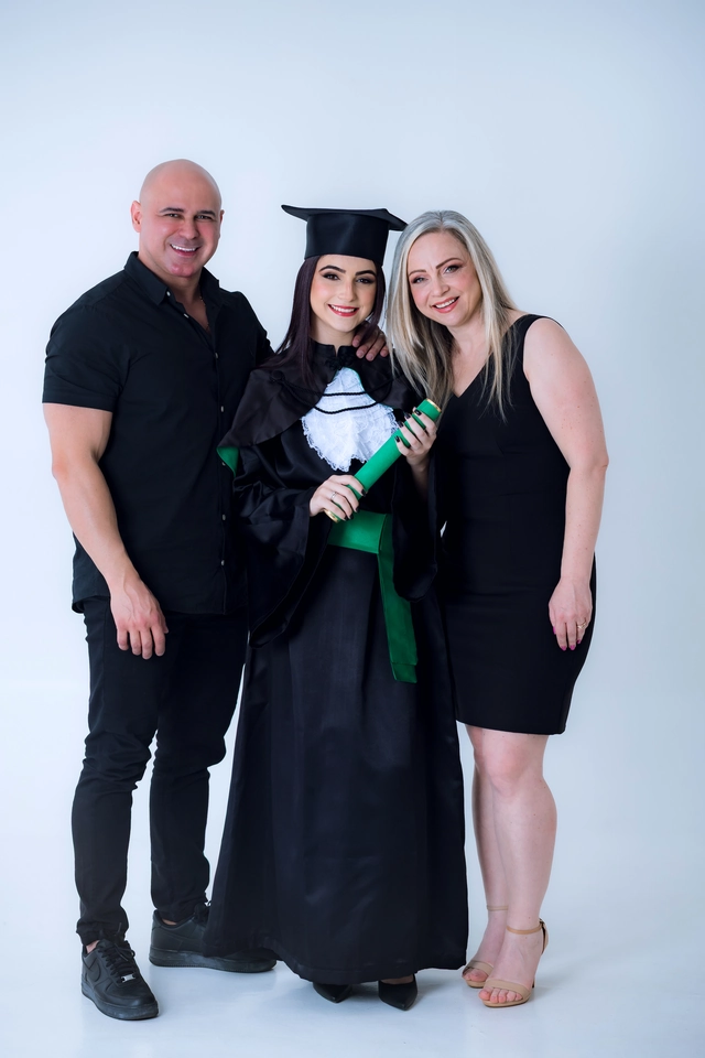Formanda segurando o diploma ao lado do pai e da mãe