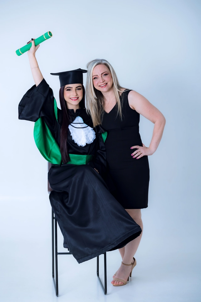 Formanda comemorando com o diploma erguido ao lado da mãe