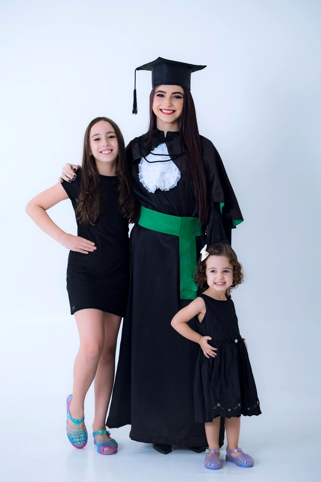 Formanda de beca e capelo ao lado das duas irmãs mais novas