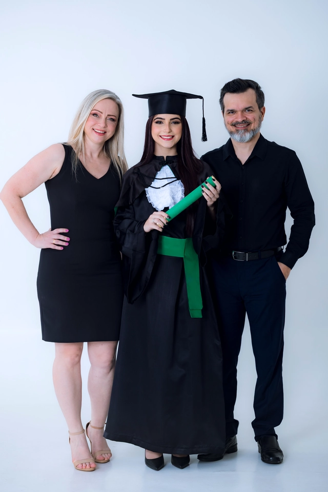 Formanda ao centro segurando o diploma, acompanhada por um casal de parentes
