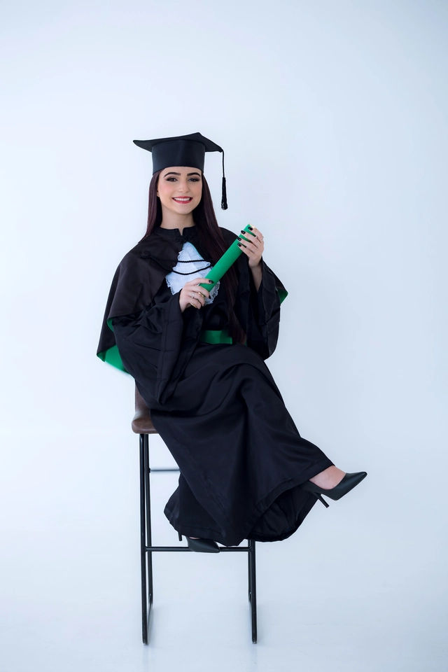 Formanda sentada no banco alto, segurando o diploma com as duas mãos
