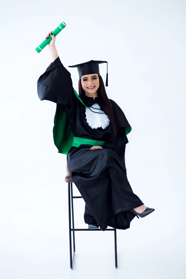 Formanda sentada no banco, erguendo o diploma com um largo sorriso