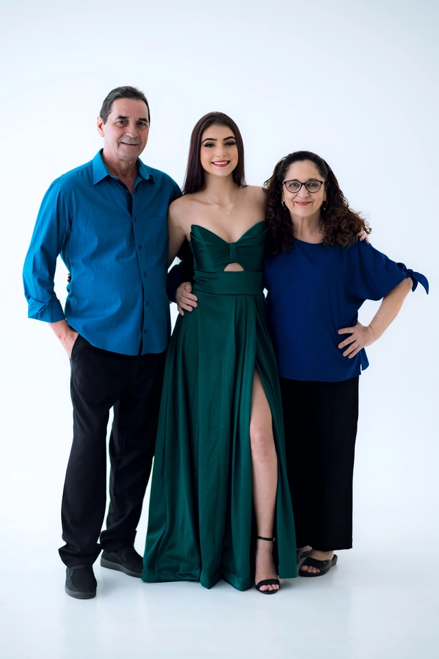 Formanda de vestido verde esmeralda entre um casal de parentes