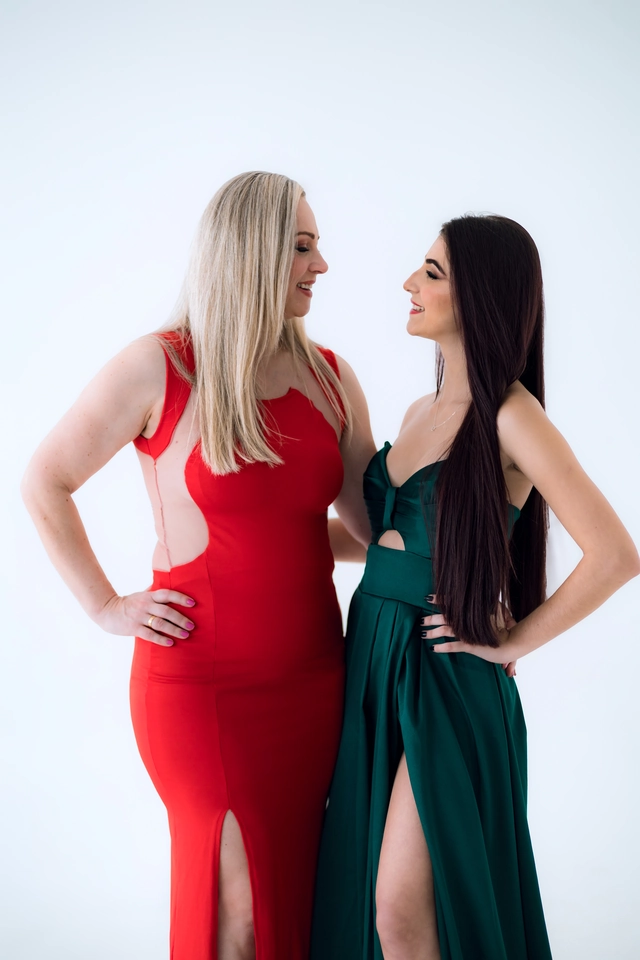 Formanda de vestido verde e parente de vestido vermelho, sorrindo rosto a rosto