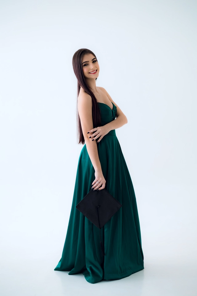 Formanda de vestido verde segurando o capelo na mão, retrato solo
