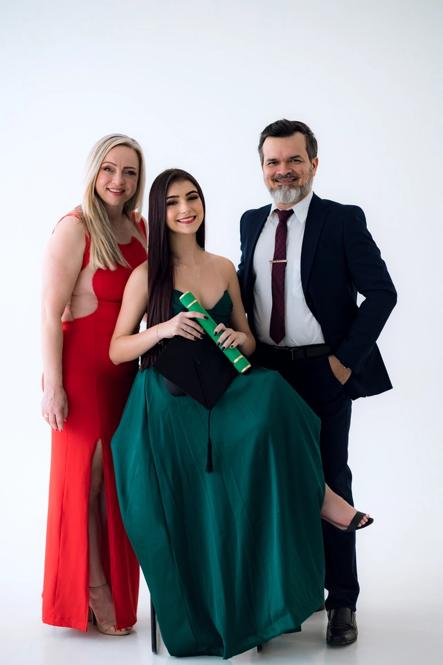 Formanda sentada segurando o diploma, entre o casal de parentes