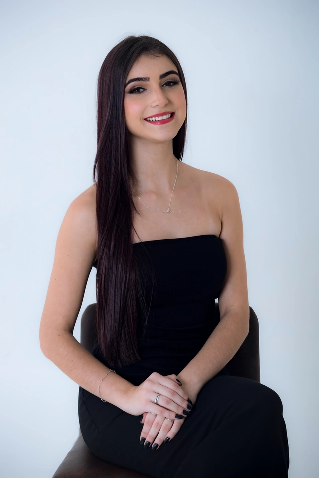 Formanda sentada de vestido preto, retrato fechado com as mãos entrelaçadas
