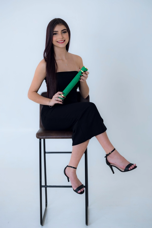 Formanda sentada de vestido preto, segurando o diploma