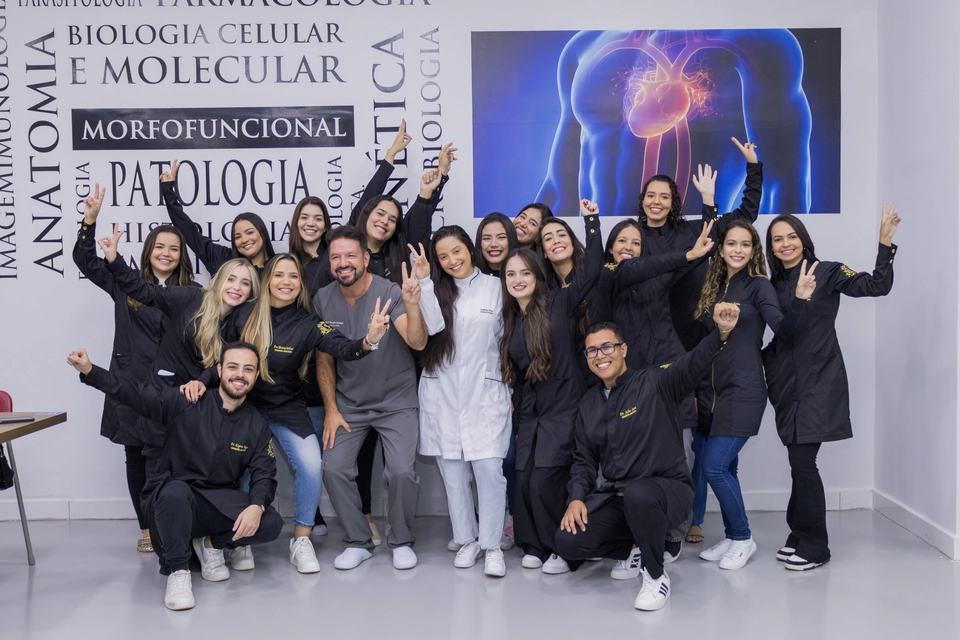 Turma completa de formandos de Odontologia reunida em sala de aula, com pôsteres de anatomia ao fundo