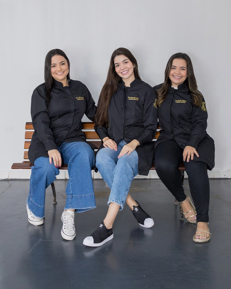 Três formandas de Odontologia sentadas num banco, sorrindo