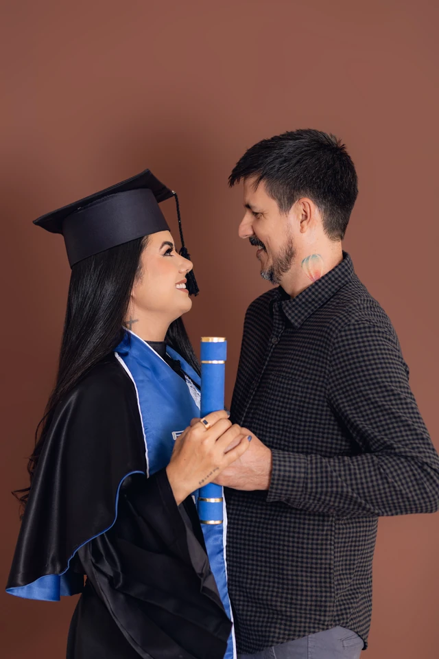 Formanda e o pai de mãos dadas, segurando o diploma, fundo marrom