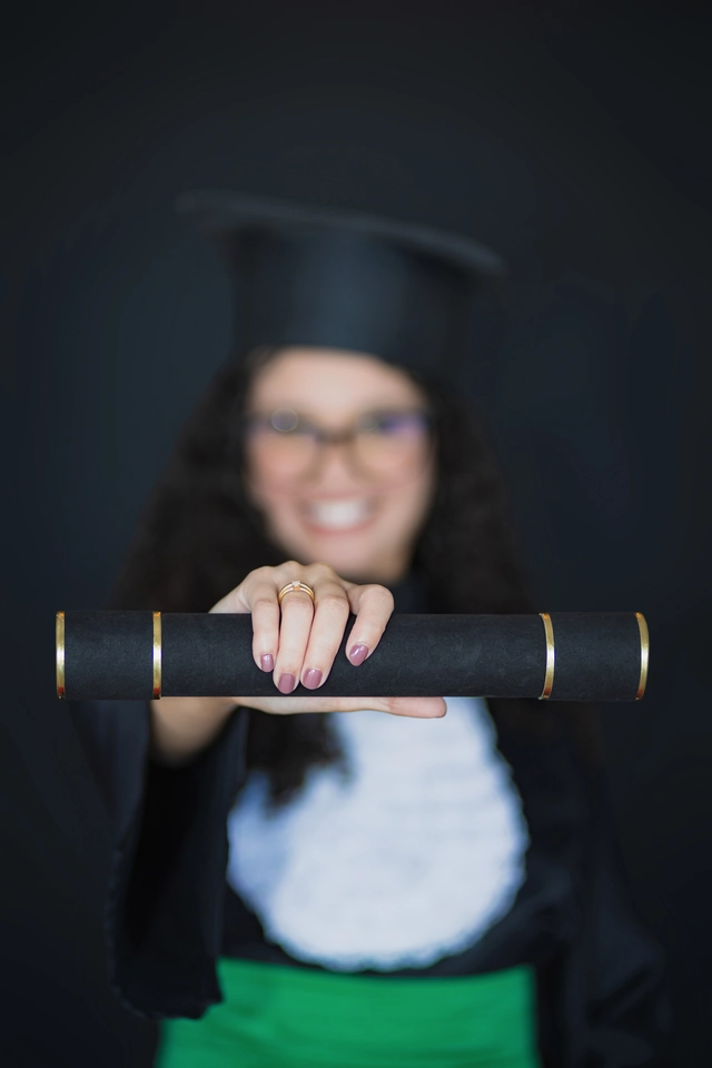Diploma em primeiro plano, com a formanda desfocada ao fundo