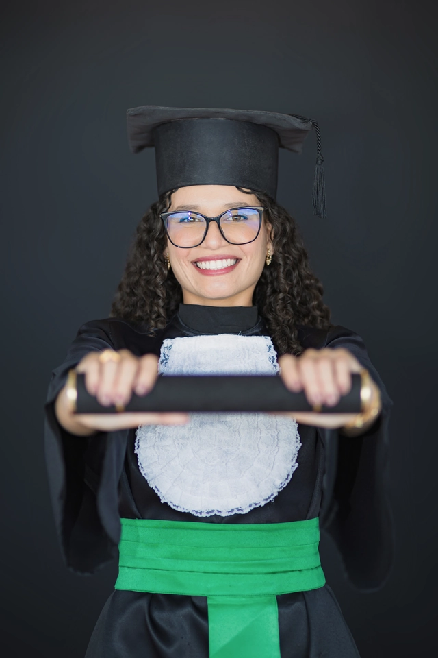 Formanda segurando o diploma com as duas mãos, sorrindo para a câmera