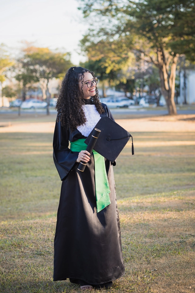 Formanda caminhando pelo campus da UFG com o capelo e o diploma nas mãos