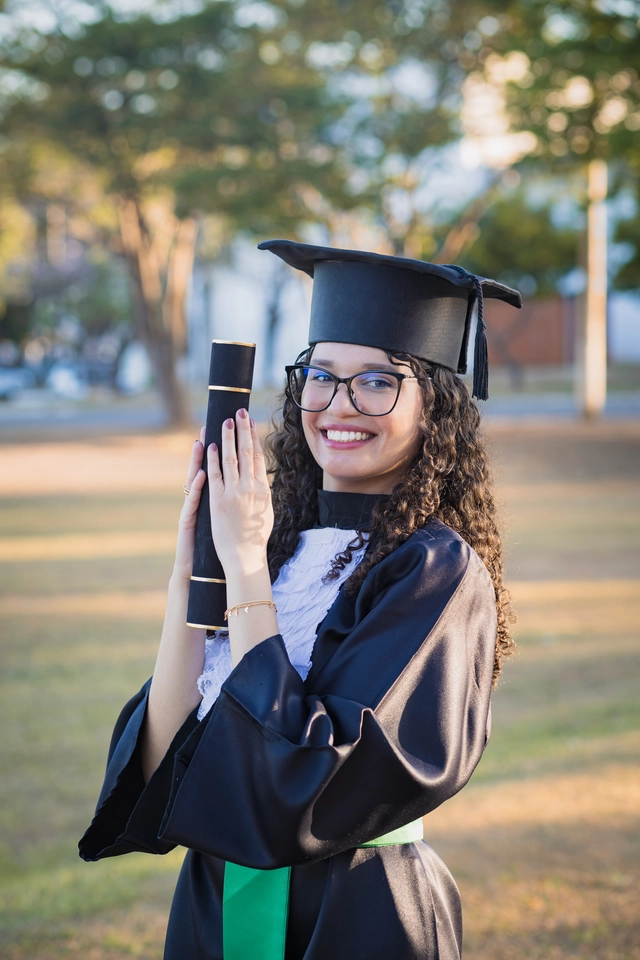Formanda sorrindo com o diploma próximo ao rosto, no campus