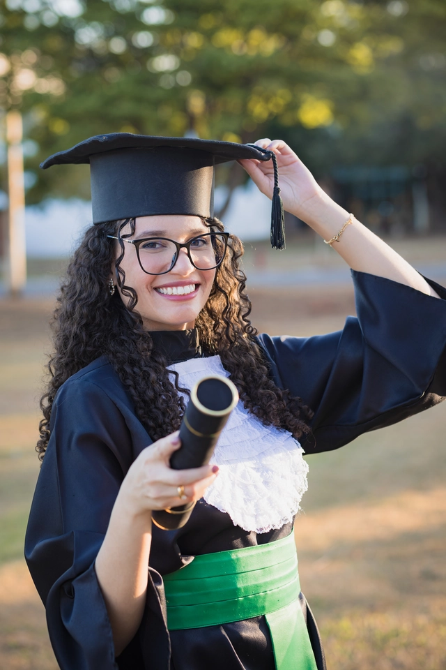 Formanda ajeitando o capelo, com o diploma na mão, no campus
