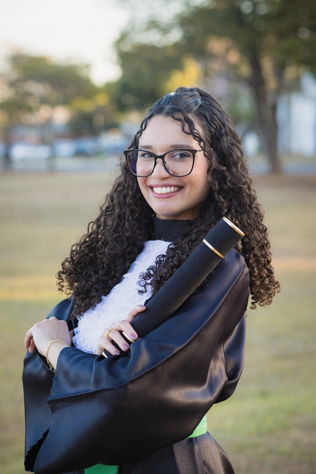 Retrato próximo da formanda sorrindo, com o campus desfocado ao fundo