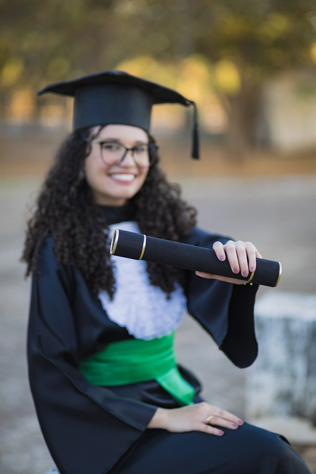 Formanda sentada, com o diploma próximo ao rosto, no campus